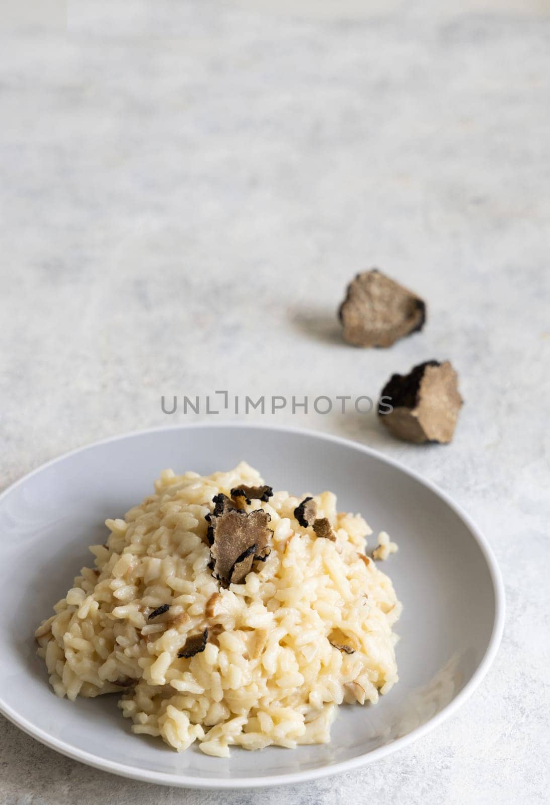 Risotto with wild porcini mushrooms and black truffles from Italy served in a plate close up on white table, copy space. Eating Italian gourmet cousine