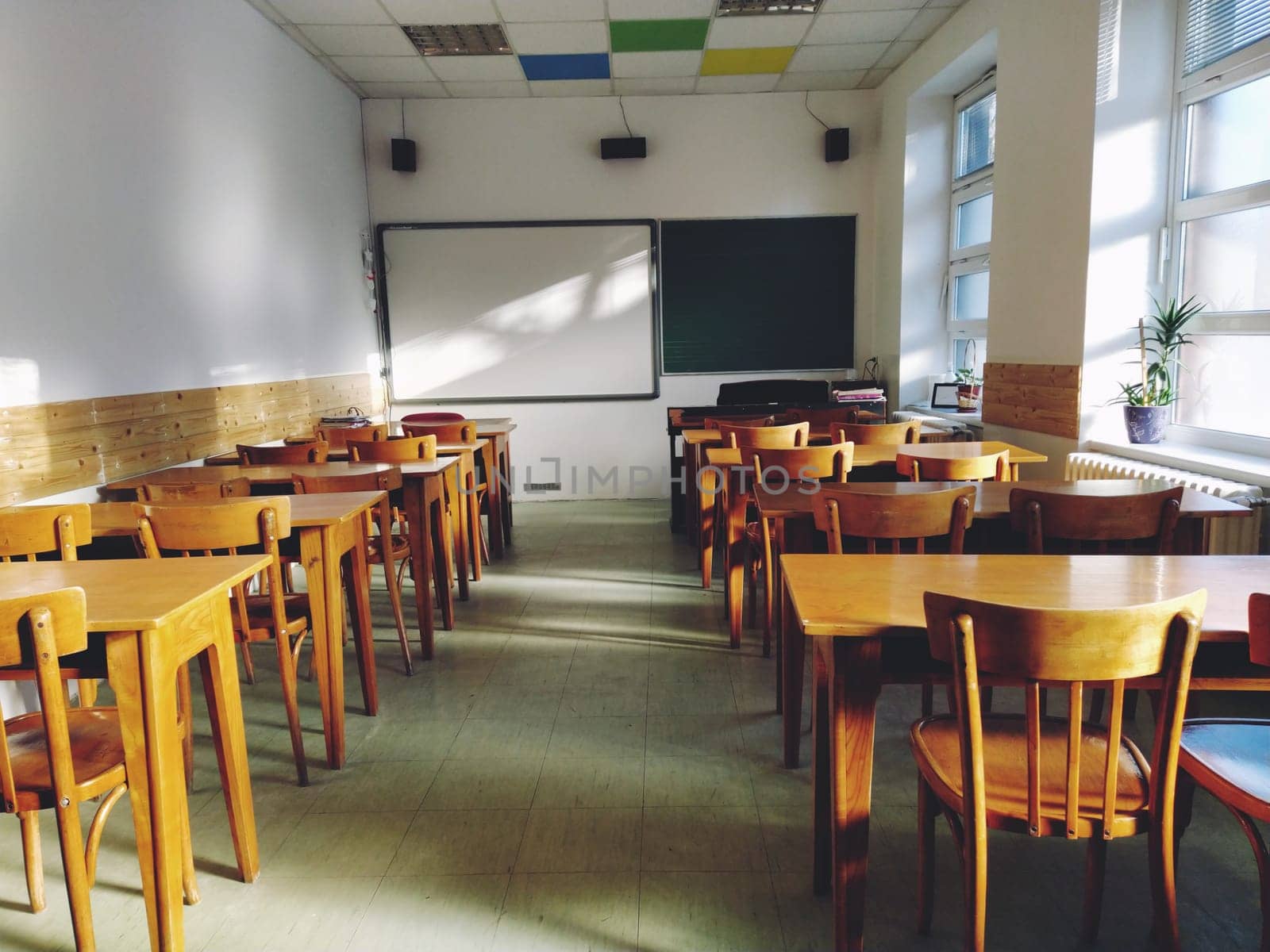 Music solfeggio empty class at school. The sun's rays fall on the floor through the window. Wooden student tables and chairs. School board and white walls. School interior