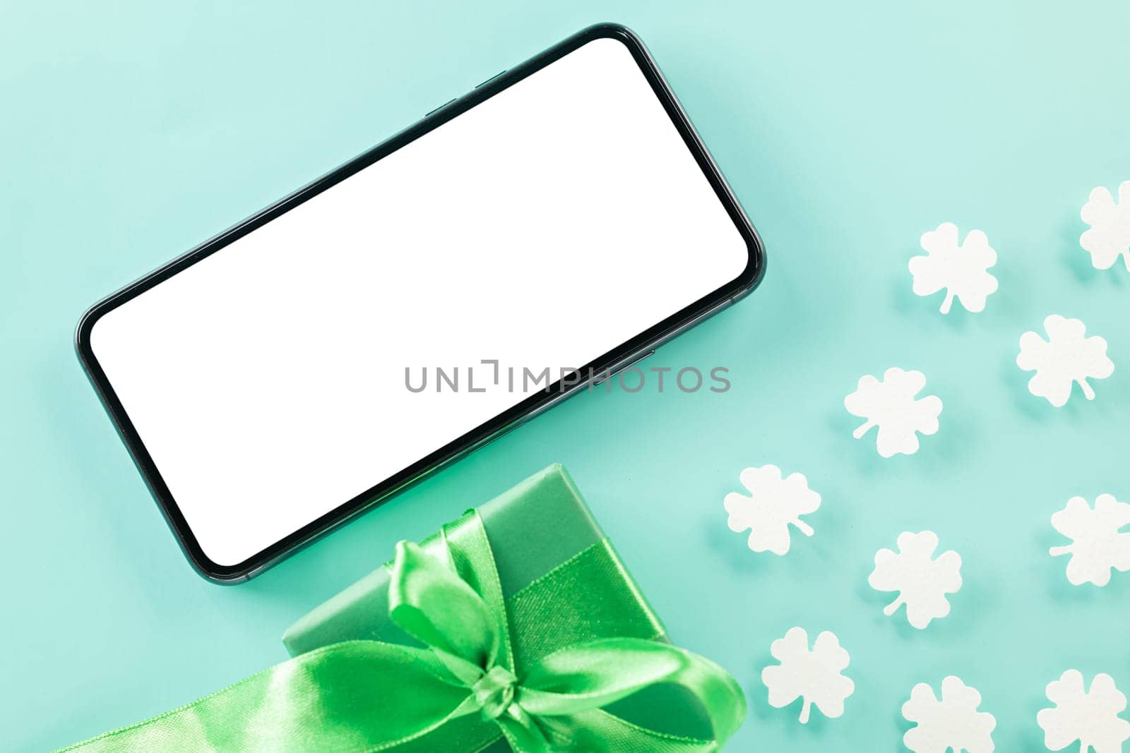 St Patricks Day. overhead flat lay of paper cut clover leaves festive decor and mobile phone blank screen, shamrocks leaf with smartphone holiday symbol on colour background, Banner greeting card