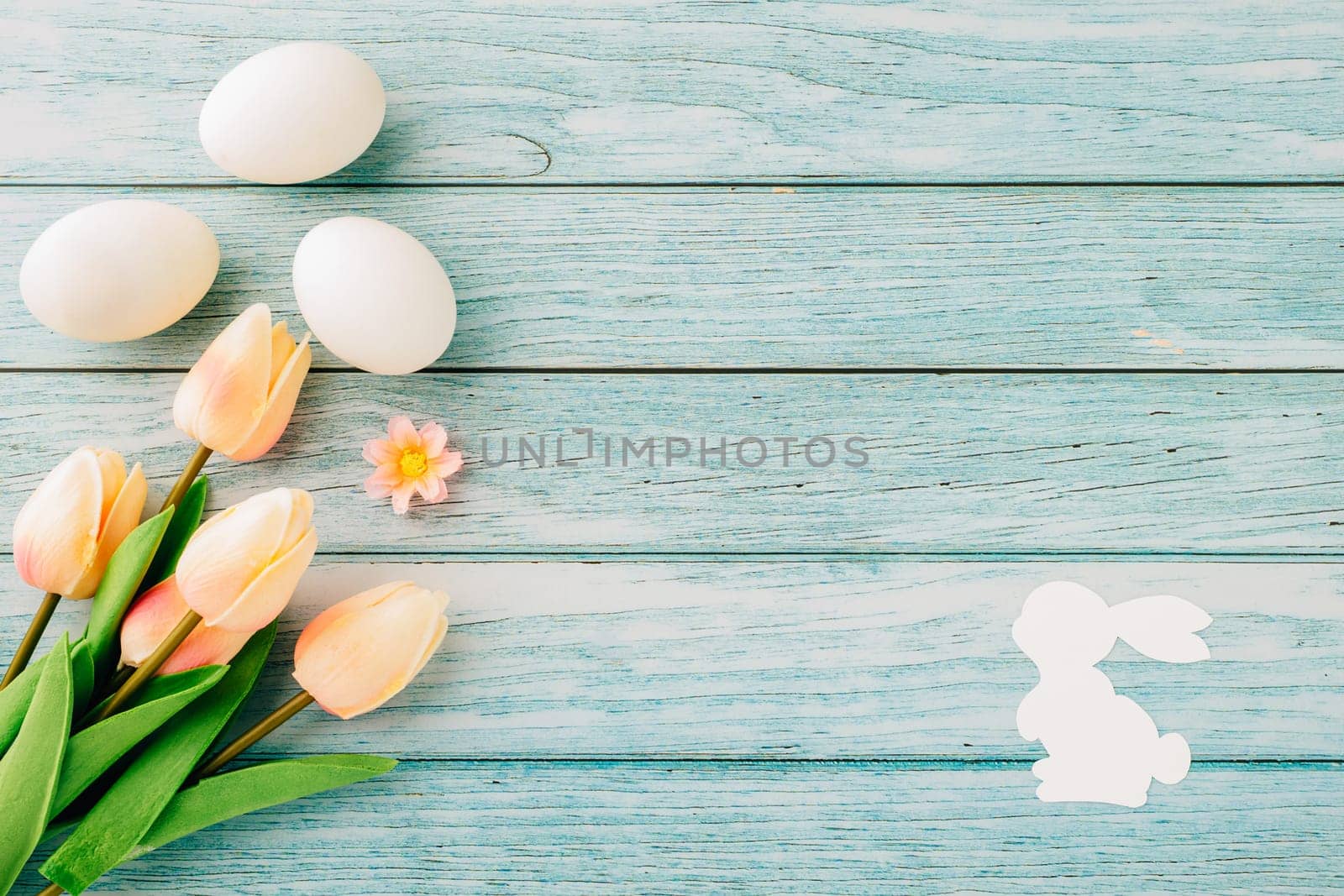 Happy Easter Day Concept. Flat lay of holiday banner background design white easter eggs and beautiful tulip flowers on blue wooden background with empty copy space, celebration greeting card