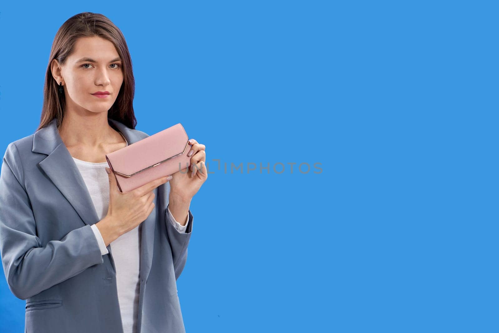 A beautiful young woman is holding a pink purse on a blue background, copy space. High quality photo