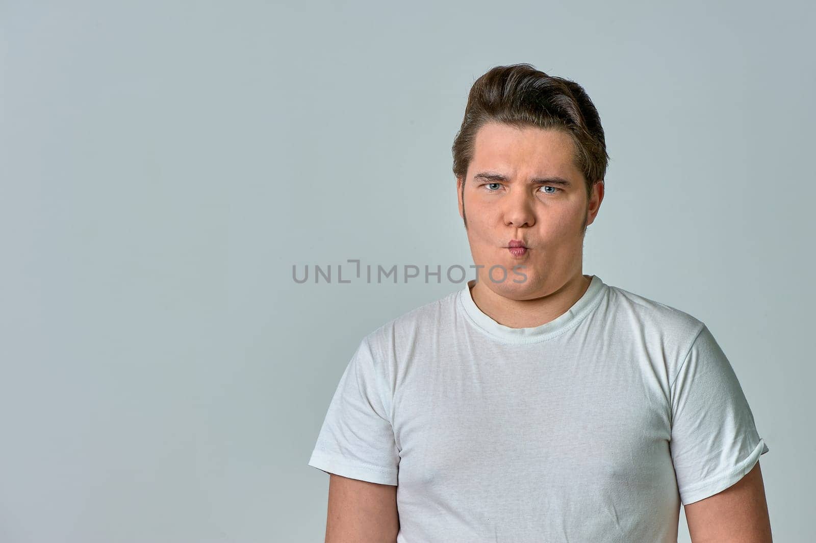a man puffing out his cheeks with a funny face on a gray background, emotions. High quality photo