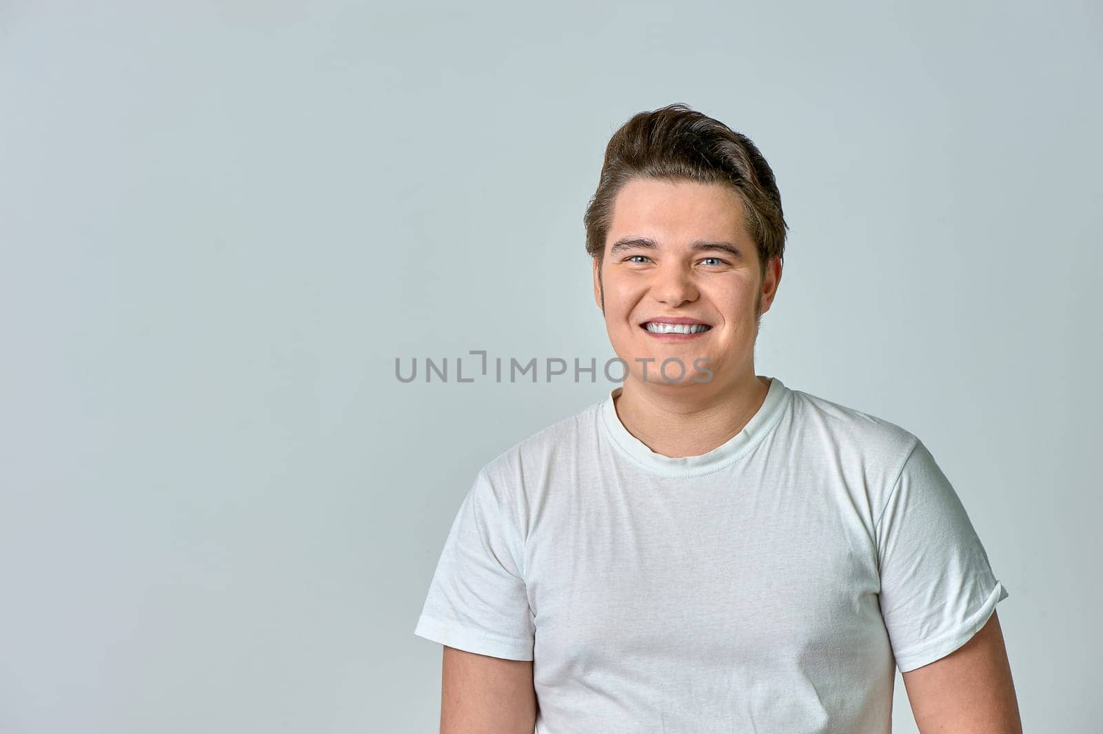 A man in a white T-shirt on a gray background smiles. High quality photo