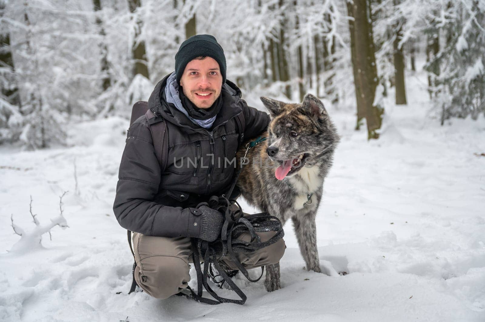 Master with his gray colored Akita Inu dog in the forest during winter with lots of snow, man is smiling and looking at camera while embracing his dog