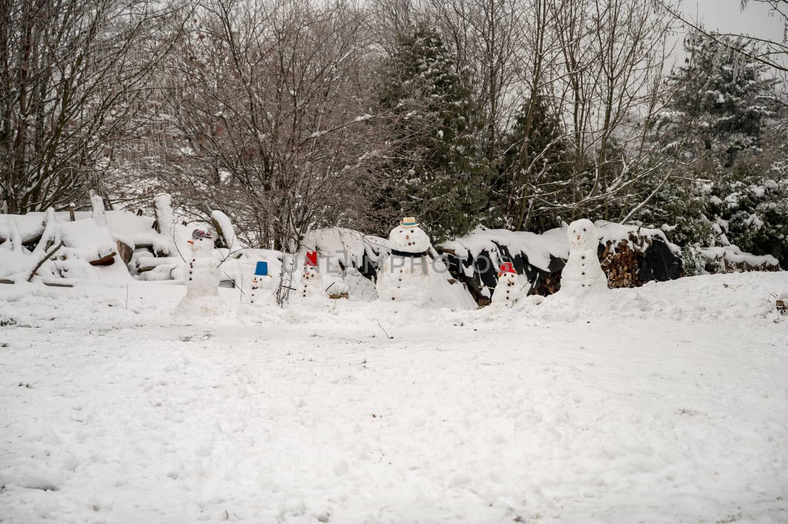 Snow man family in the snow during winter with forest in background