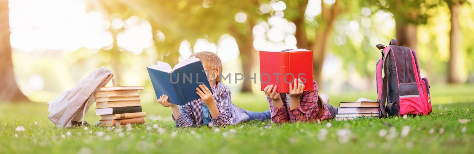 Children lying down on the green field with books in their hands. Concept of the learning, hobby and reading.