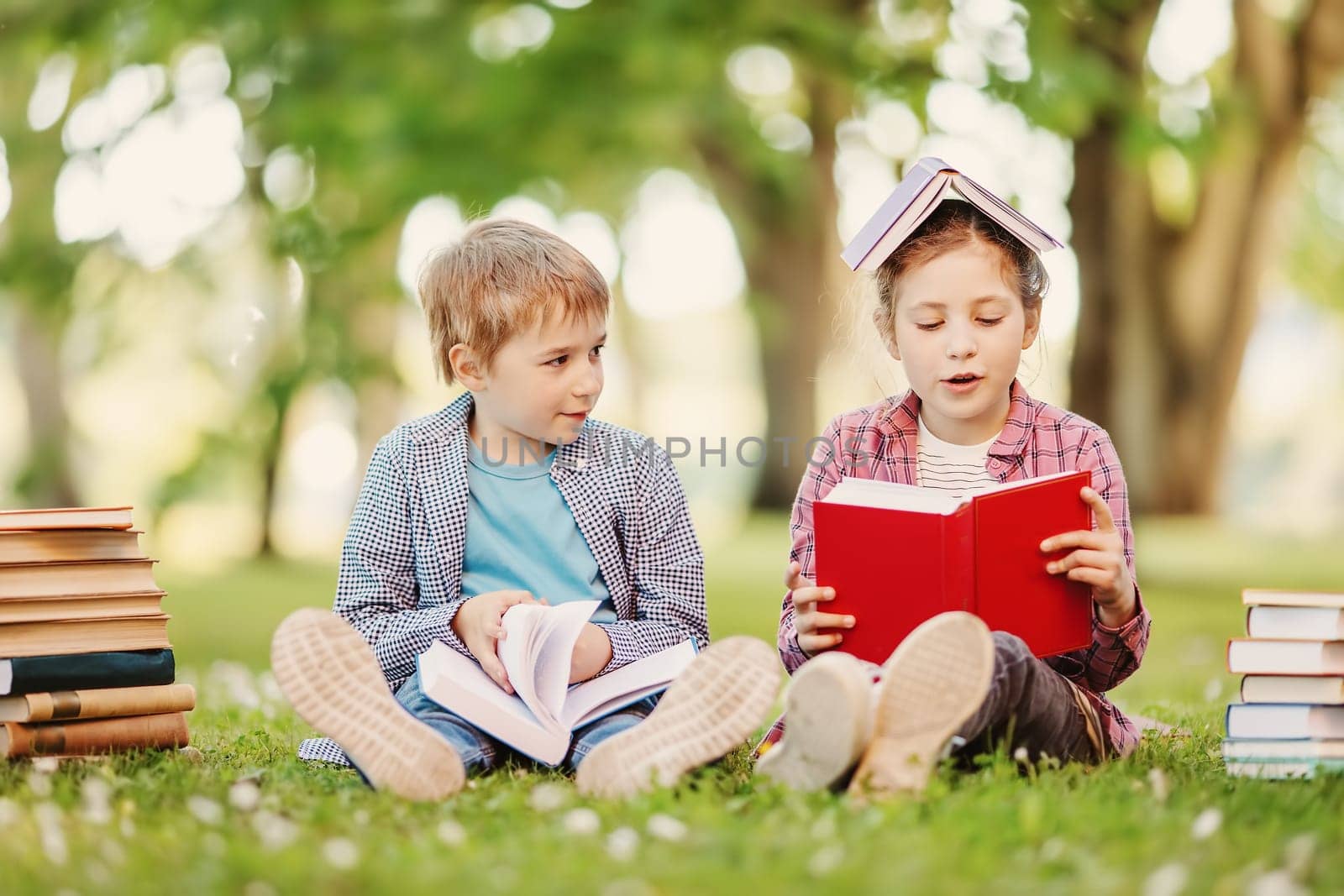 Boy and girl sitting on the meadow with books in their hands. Concept of the back to school and hobby.