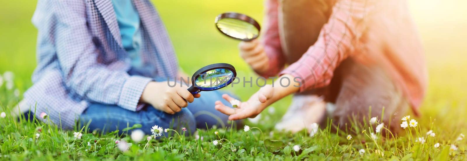 Children exploring fresh nature by using magnifying glasses. Concept of the family, vacation and recreation.