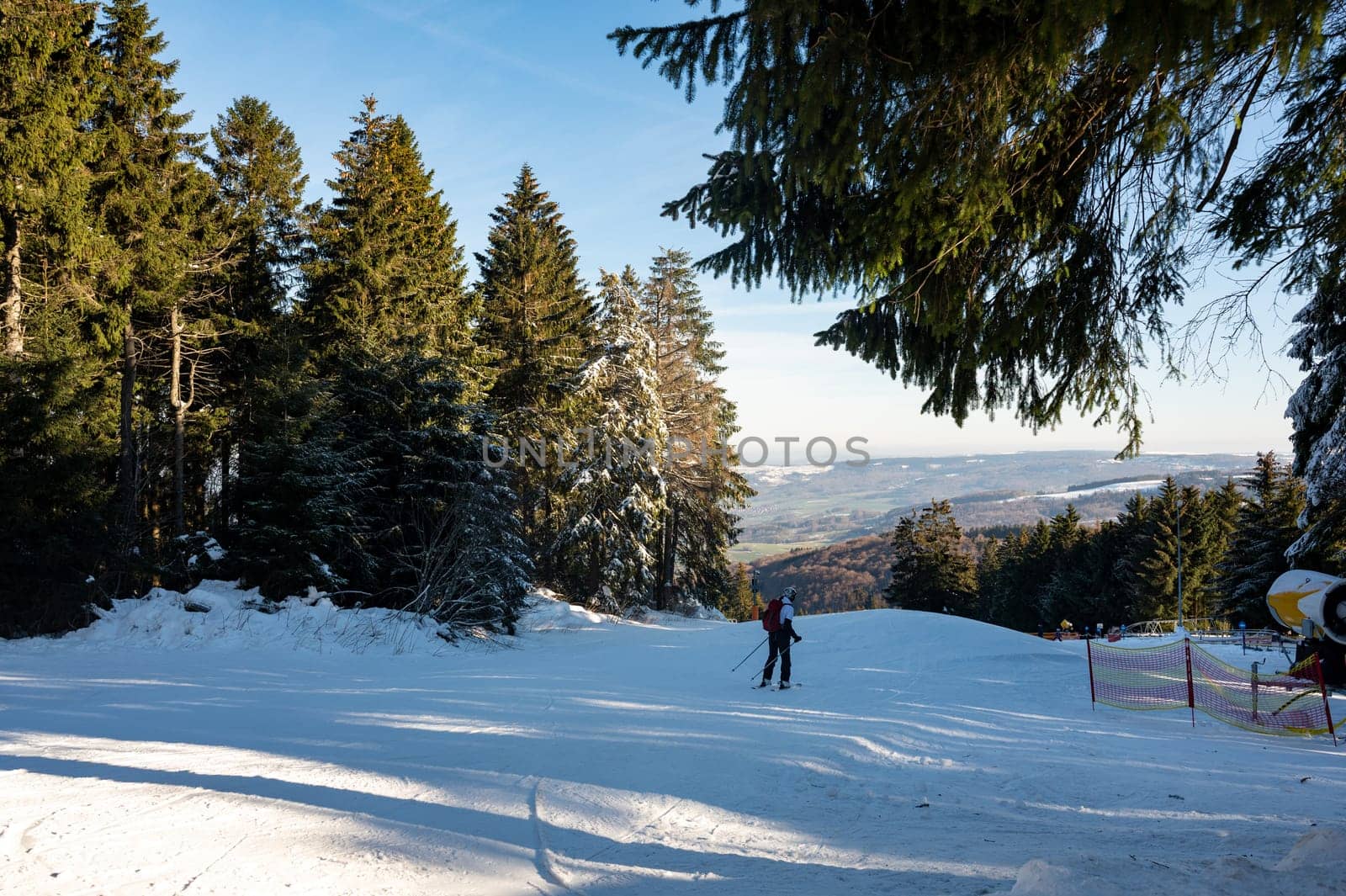 Ski slope on the Wasserkuppe with skiers, snow cannon on the side and with blue sky and trees