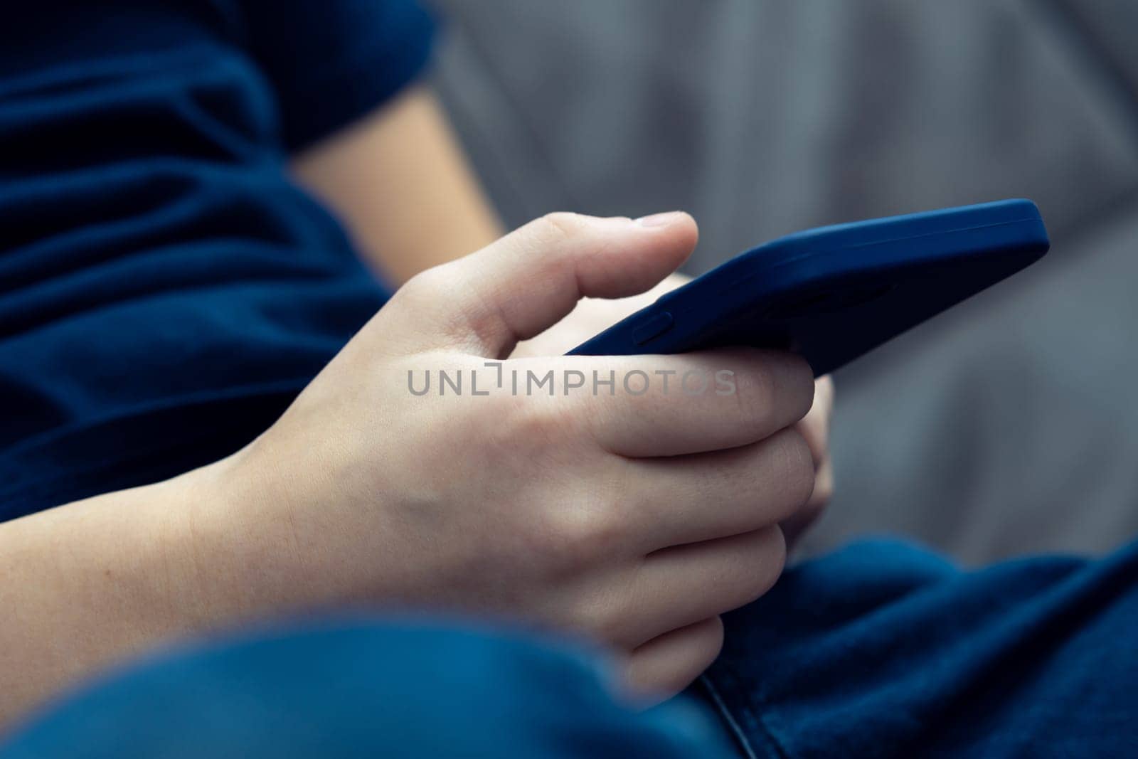 Close up unrecognizable male hands holding smartphone in blue mobile case, sitting on sofa. Trading and marketing occupation, checking bills and electronic commerce. Internet and web technology.