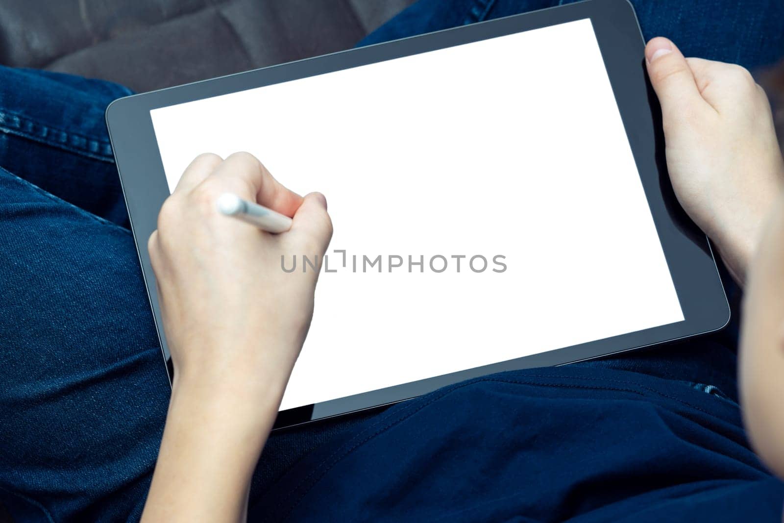 Unrecognizable male hands drawing with stylus pen on digital tab, pad touchscreen with white screen on knees. Web technology and app for artists, creative occupation online. High angle, above shoulder