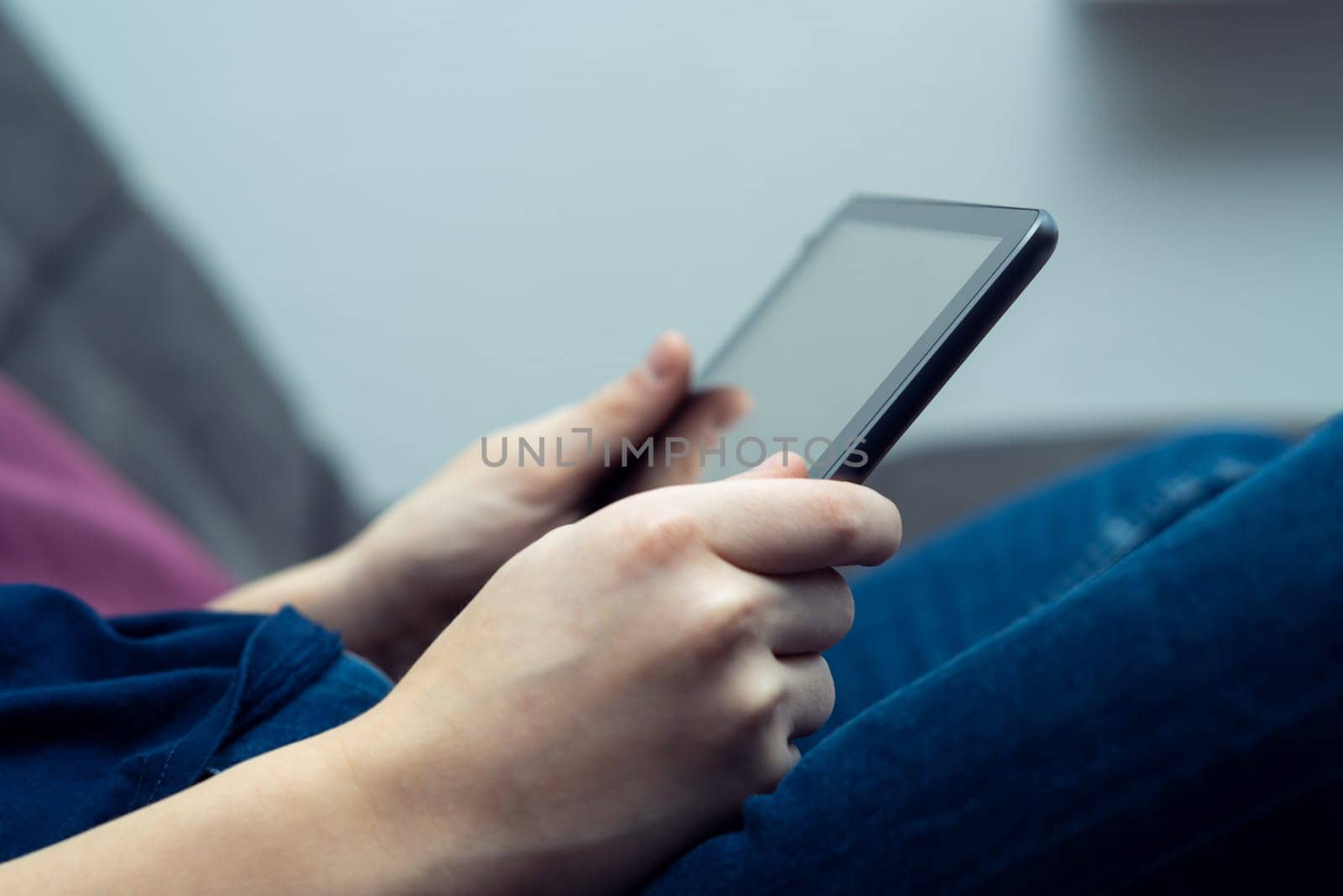 Cropped teenage boy hands holding digital tablet, watching movies or new, sitting on sofa. Internet and technology for streaming services. Chatting with friends, social media and smart applications.