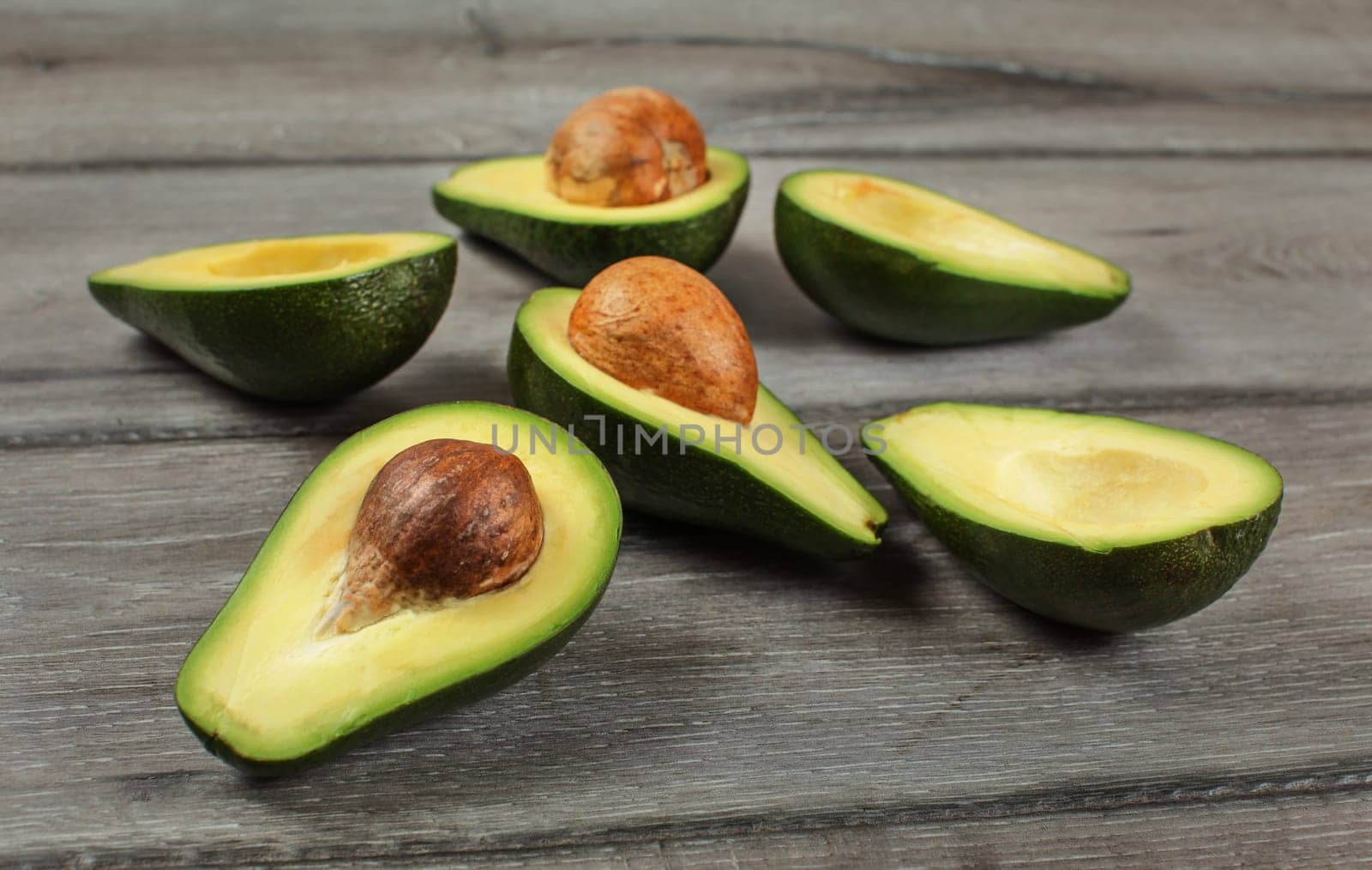 Avocados cut in half, seed visible, on gray wood desk.