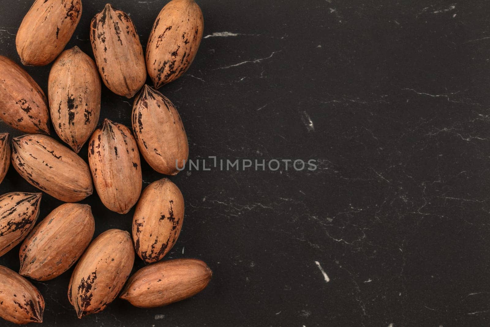 Tabletop view, whole pecan (Carya illinoinensis) nuts with spots on shells (Turkish variety) on black marble desk, space for text on right side.
