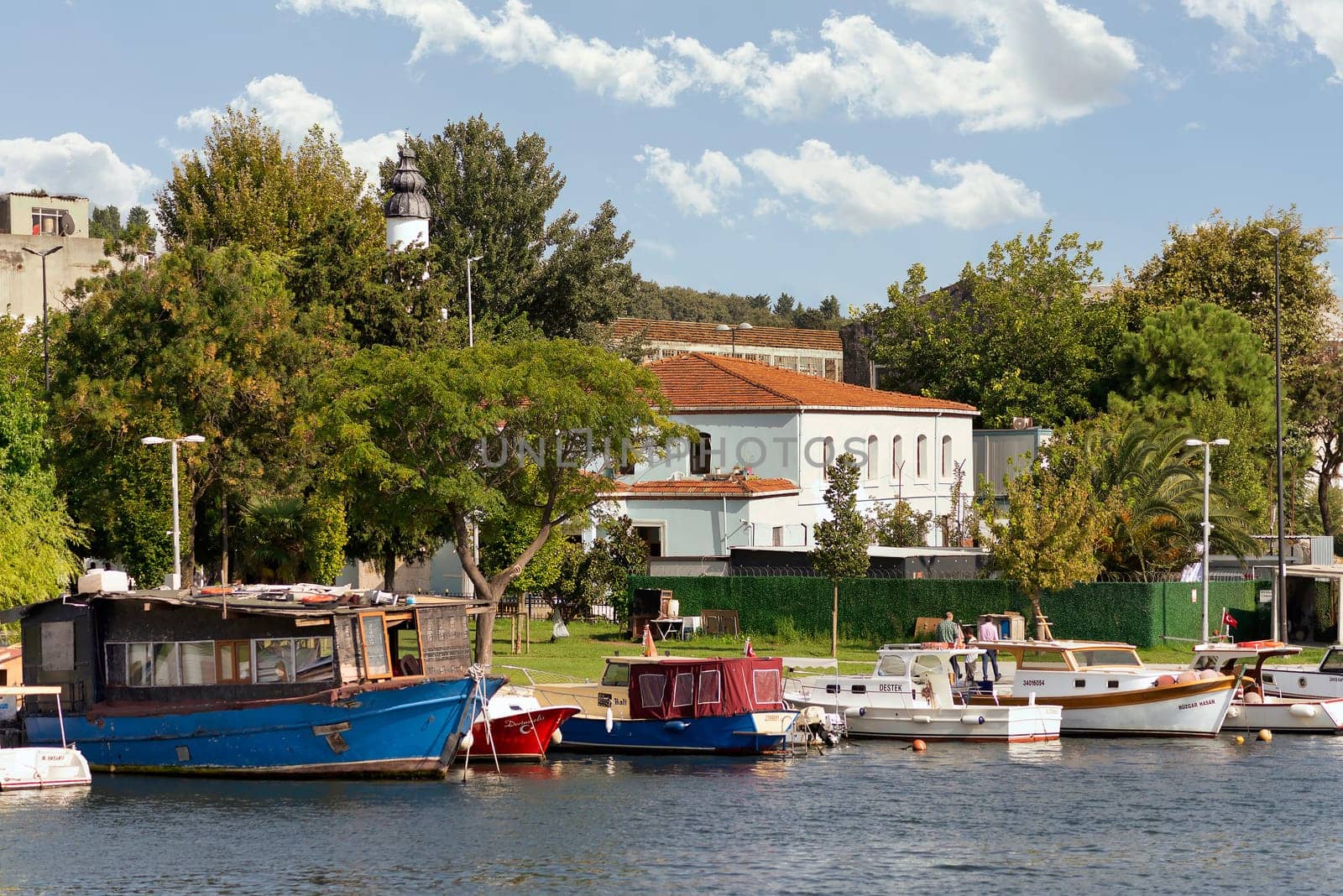 Istanbul, Turkey - September 1, 2022: Boats docked at the coast of the Golden Horn, with background of green park with dense big trees, and residential houses, in a sunny summer day