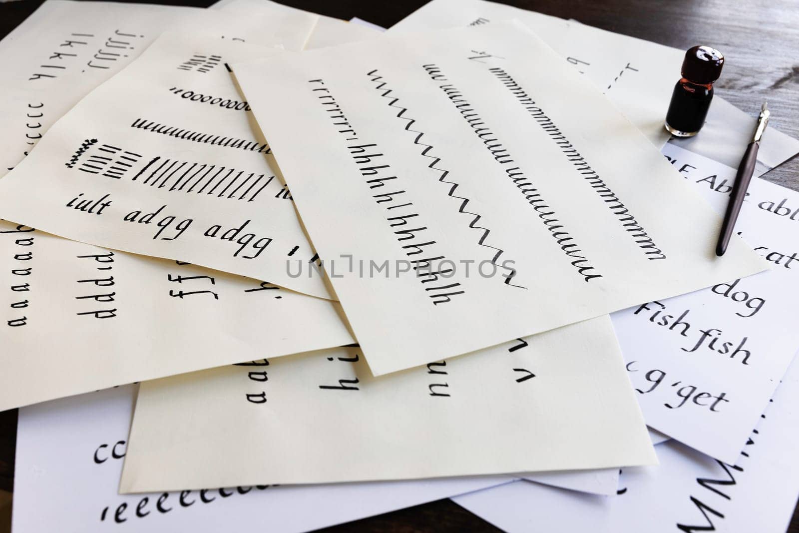 Calligraphy practice pages scattered on a table with dip pen and small bottle of ink