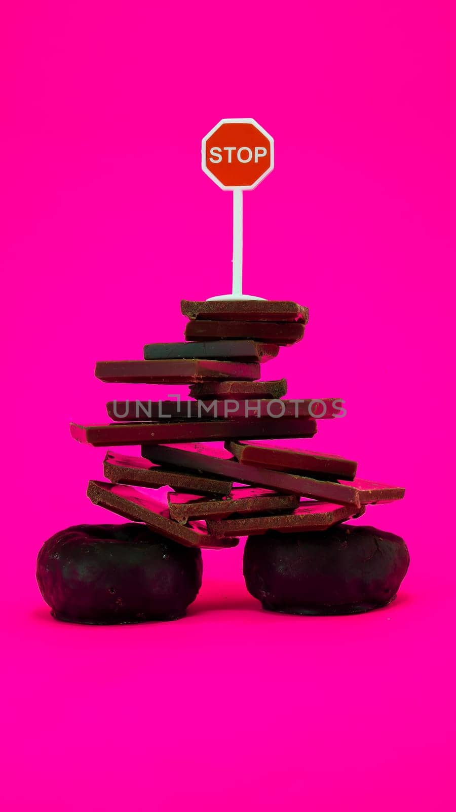Chocolate and donuts isolated on pink background with stop sign on top