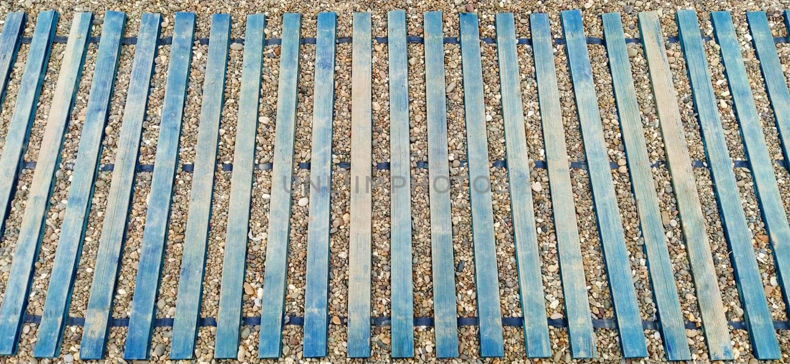 Wooden boardwalk on the beach. Sticks and boards on rocky ground. Heel protection from damage. Summer time and beach holidays. Travel and tourism concept.