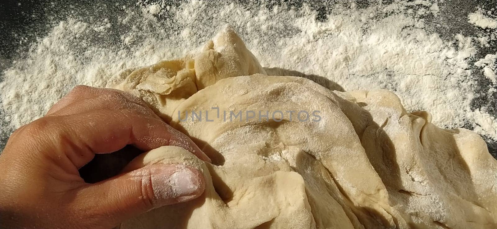 Hands knead the dough. The woman kneaded dough for baking or dumplings. Preparation of flour, water and egg mass for thermal processing. Chef hands.