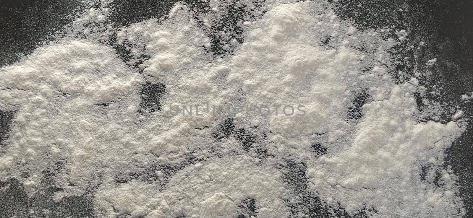 White wheat flour, sifted and sprinkled on a black background. Preparation for baking. Close up and selective focus.