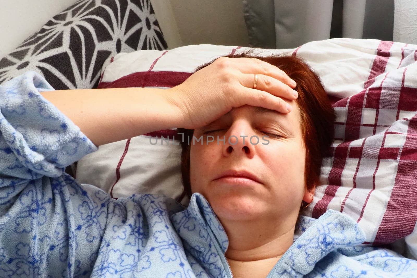 Sick woman in bed. Headache, runny nose and cold. Paleness of the face and faintness of the body. Feeling unwell. The patient holds his forehead with his hand and covers his eyes.