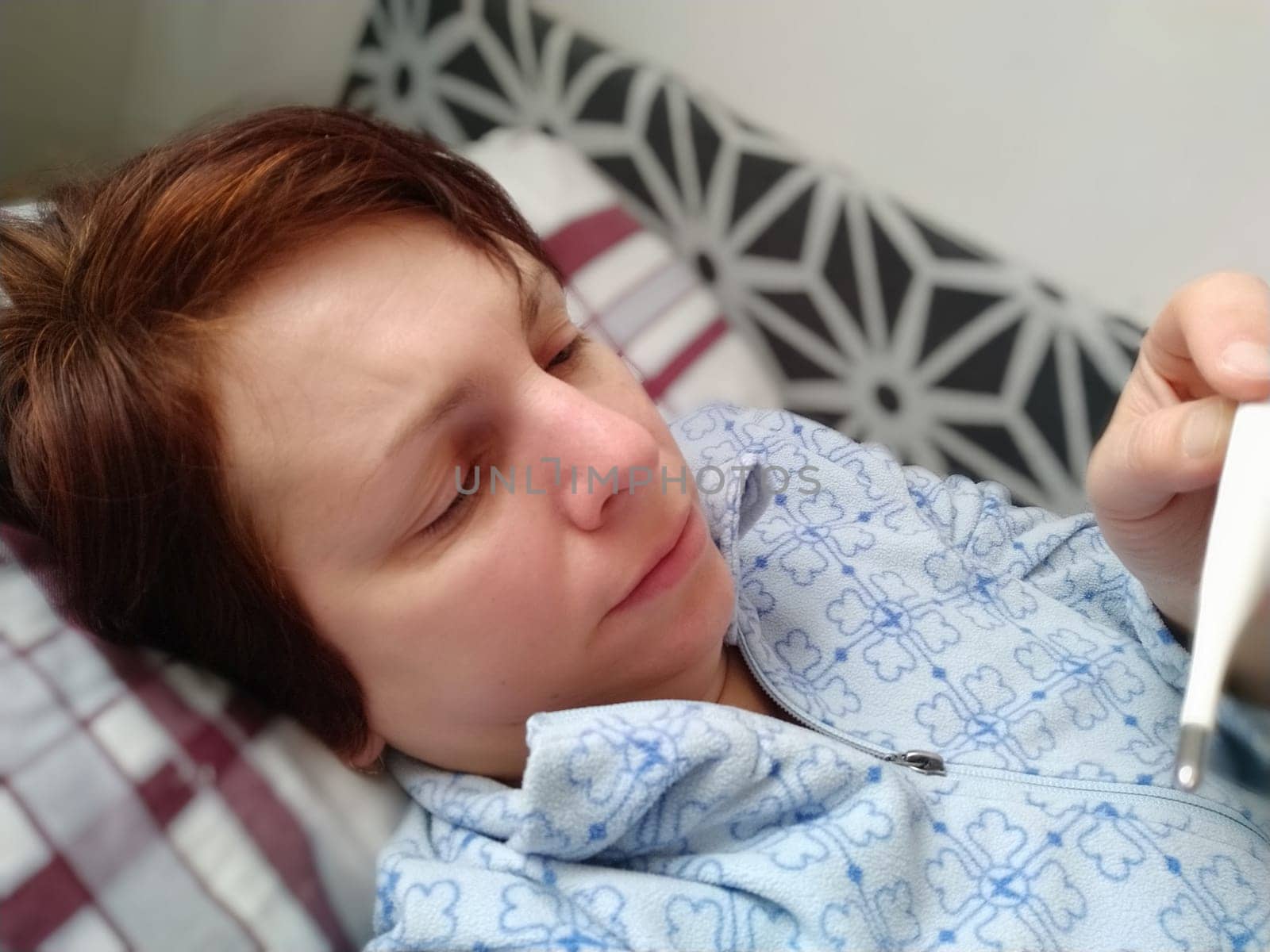 Sick woman in bed. Headache, runny nose and cold. Paleness of the face and faintness of the body. Feeling unwell. The patient lies on a pillow, holds a thermometer and measures the temperature