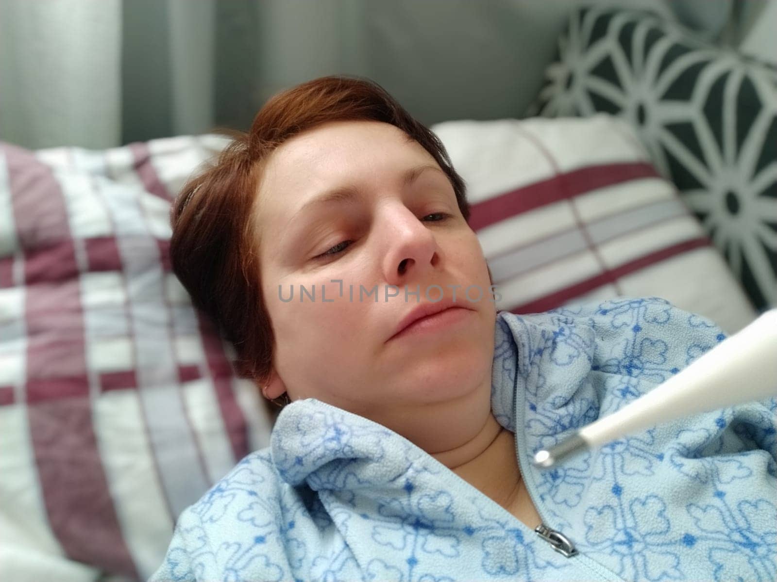 Sick woman in bed. Headache, runny nose and cold. Paleness of the face and faintness of the body. Feeling unwell. The patient lies on a pillow, holds a thermometer and measures the temperature