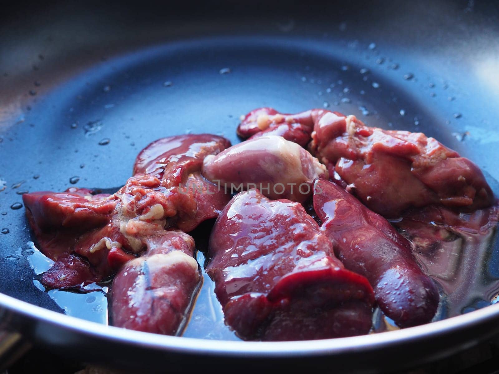 chicken liver, kidney and heart in a non-stick skillet. The offal of the bird is placed in a dark bowl and sprinkled with vegetable oil. Cooking food high in heme iron. Anti-anemic diet.