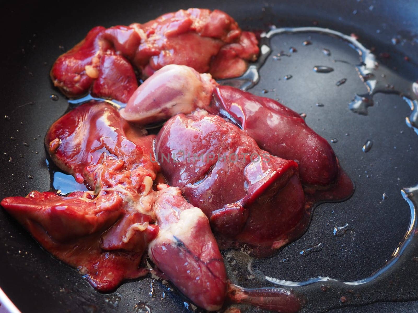 chicken liver, kidney and heart in a non-stick skillet. The offal of the bird is placed in a dark bowl and sprinkled with vegetable oil. Cooking food high in heme iron. Anti-anemic diet.