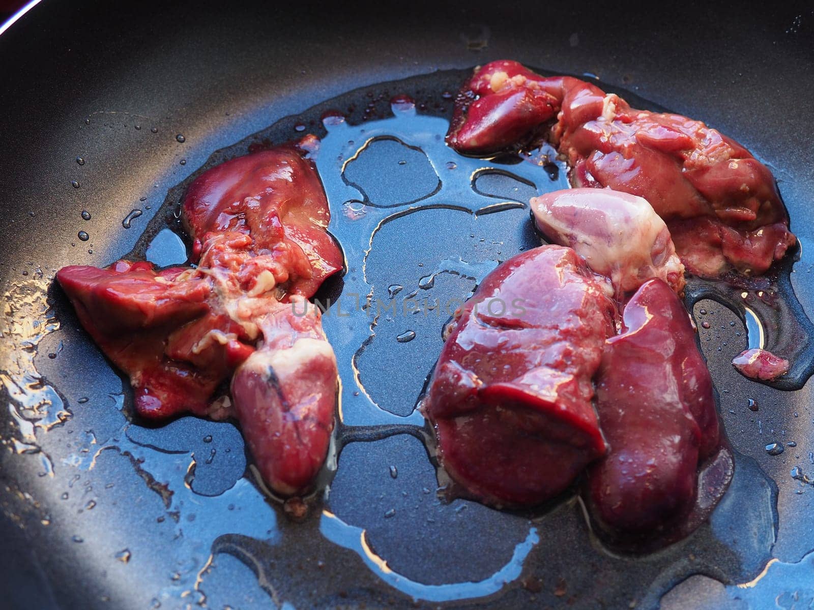 chicken liver, kidney and heart in a non-stick skillet. The offal of the bird is placed in a dark bowl and sprinkled with vegetable oil. Cooking food high in heme iron. Anti-anemic diet.