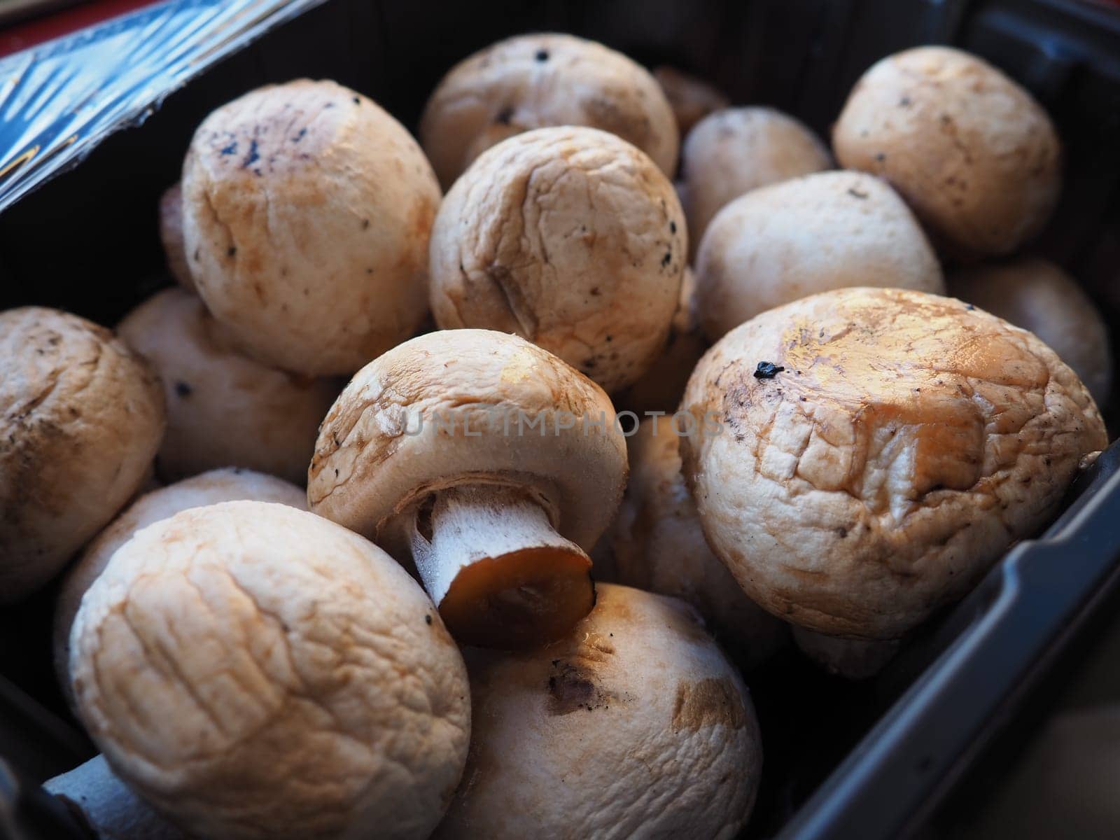 champignons in black plastic packaging. Brown champignons grown in a mushroom factory. Mushrooms in an opened store packaging. Close-up of mushrooms after defrosting. Shelf life of food