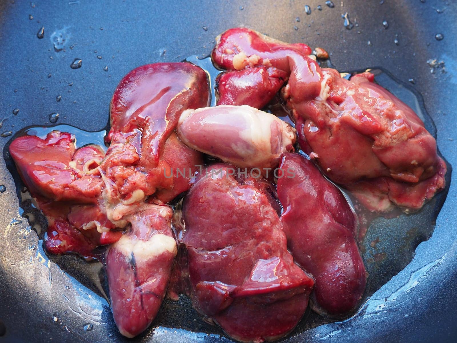 chicken liver, kidney and heart in a non-stick skillet. The offal of the bird is placed in a dark bowl and sprinkled with vegetable oil. Cooking food high in heme iron. Anti-anemic diet.