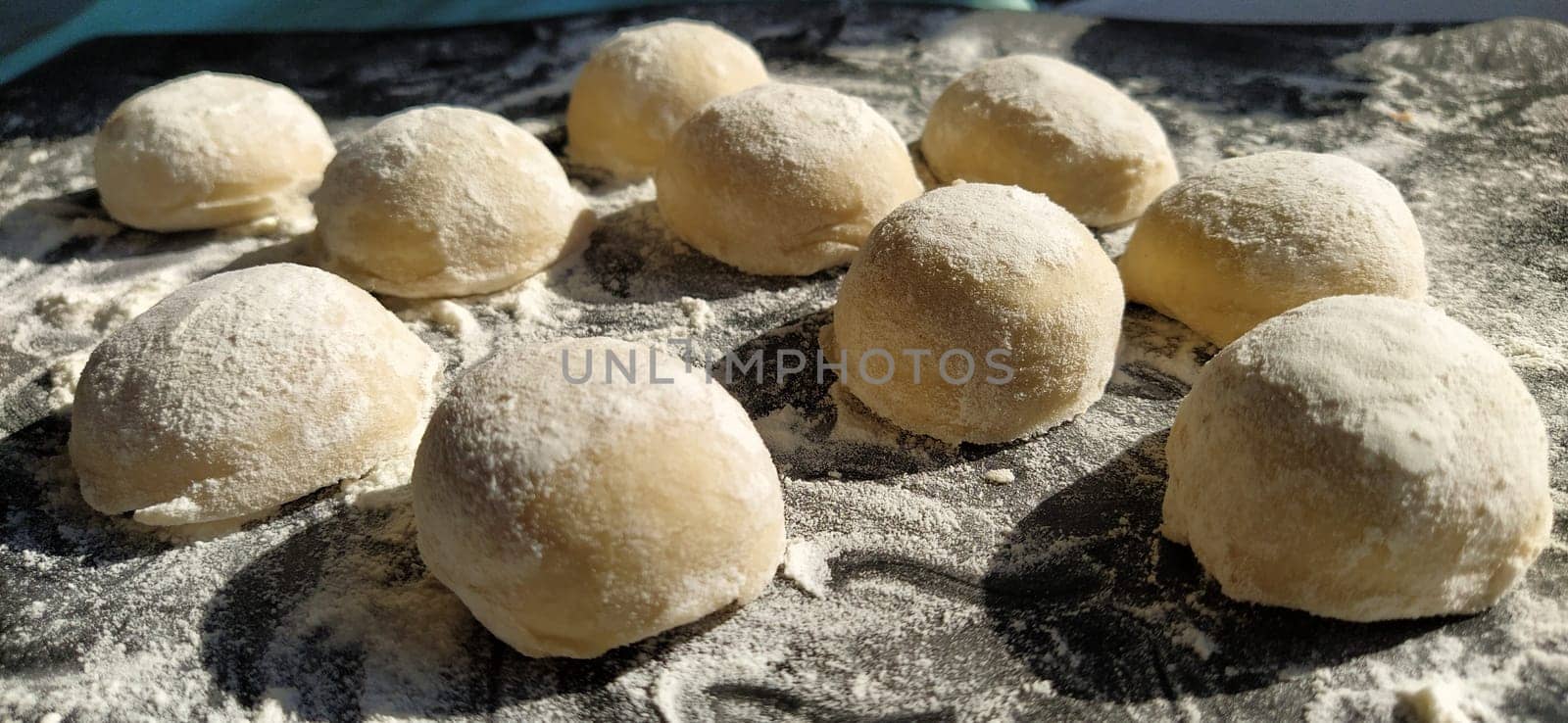 Round pieces of shortbread dough for making cookies or gingerbread. Raw buns or dumplings with scattered flour around on black background.