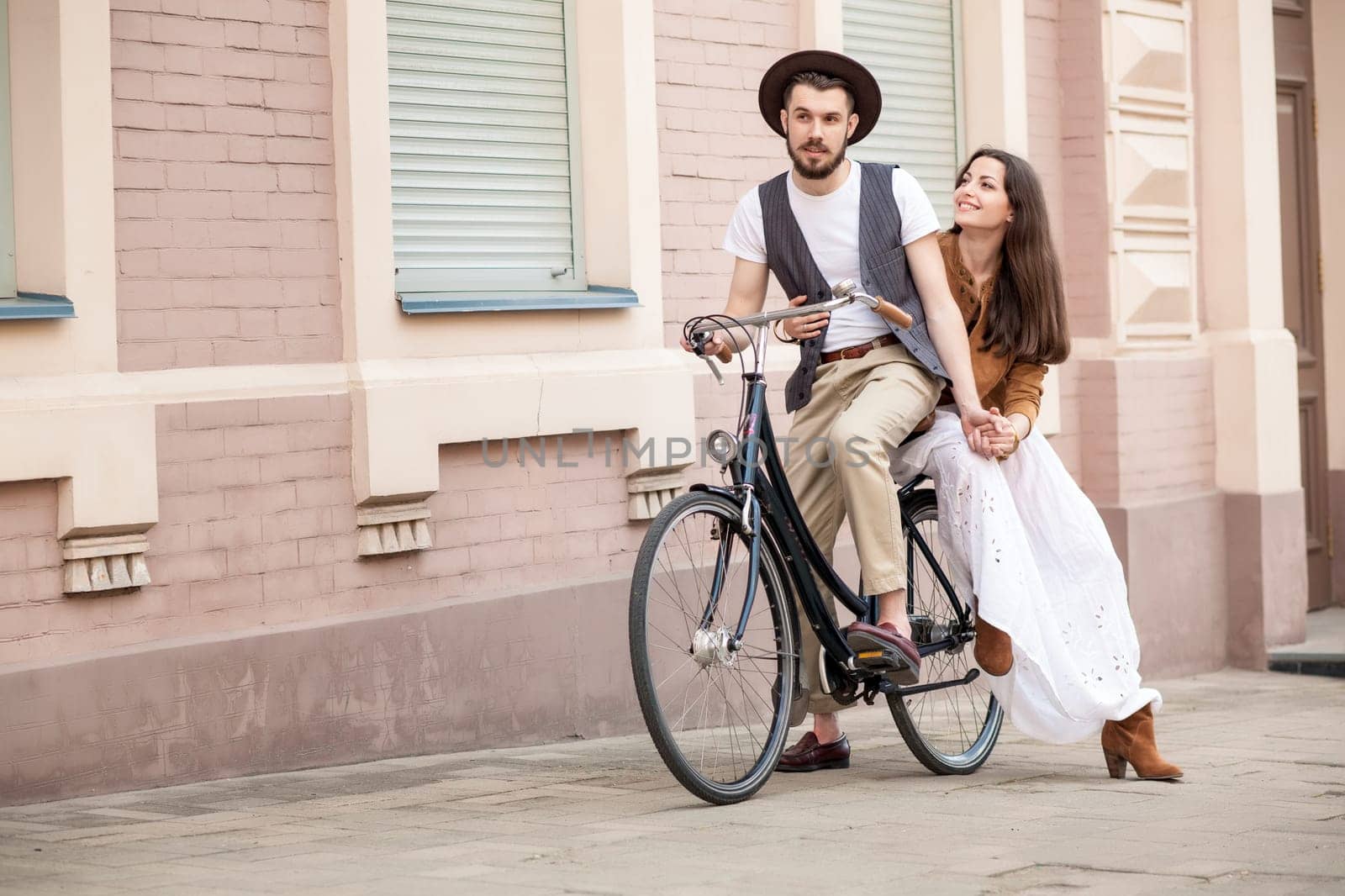 Young couple sitting on a bicycle against the wall in town