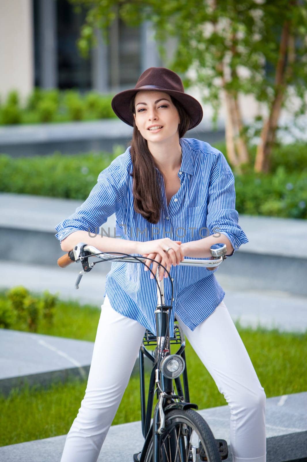 Pretty smiling girl in hat and blue dress riding a bicycle at street lifting legs
