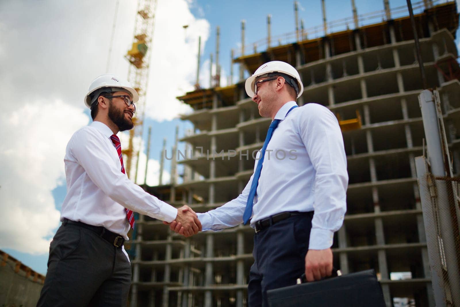 Two architects handshaking on background of new construction