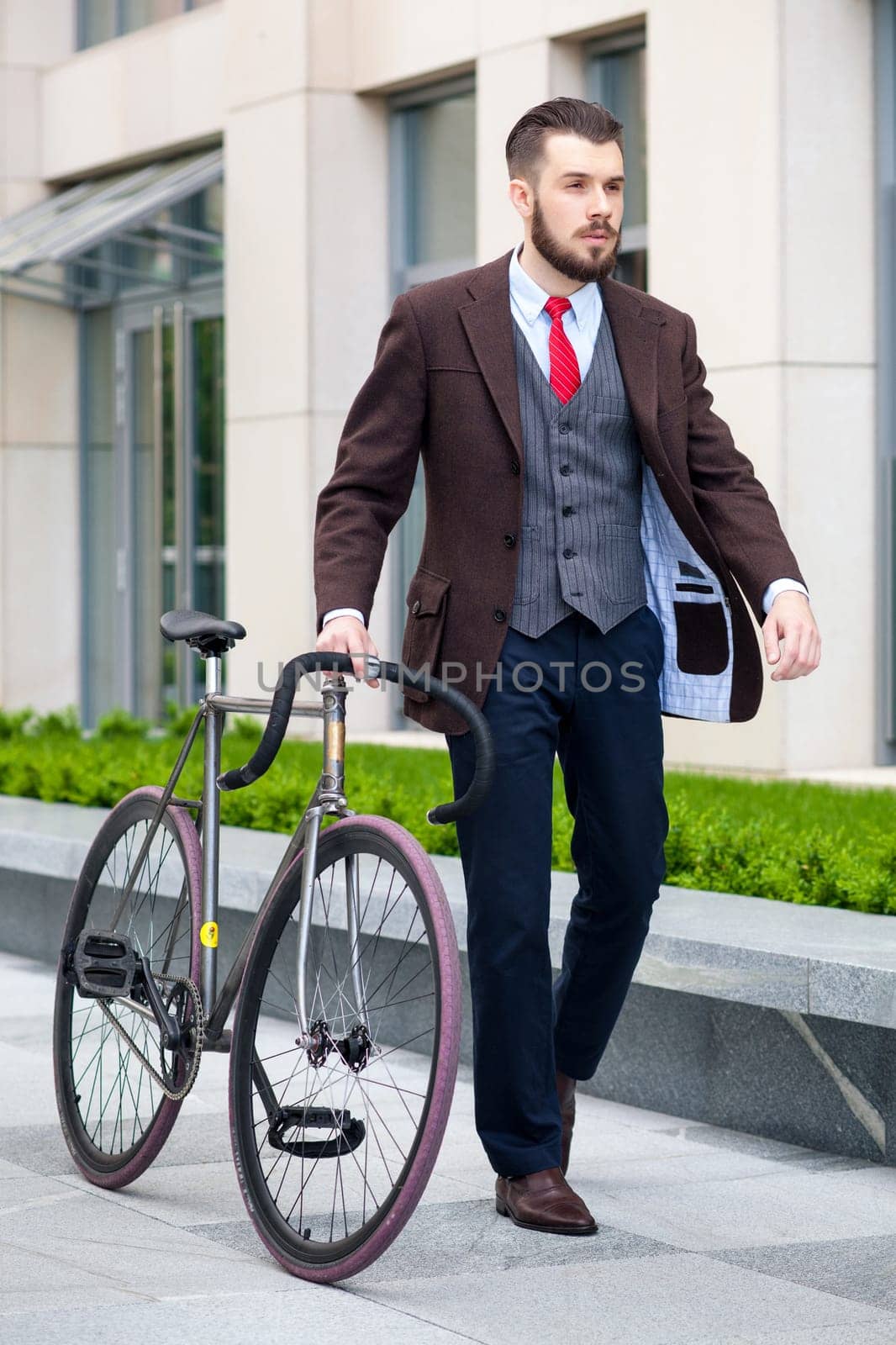 Handsome businessman in a jacket and red tie and his bicycle on city streets. The concept of the modern lifestyle of young men