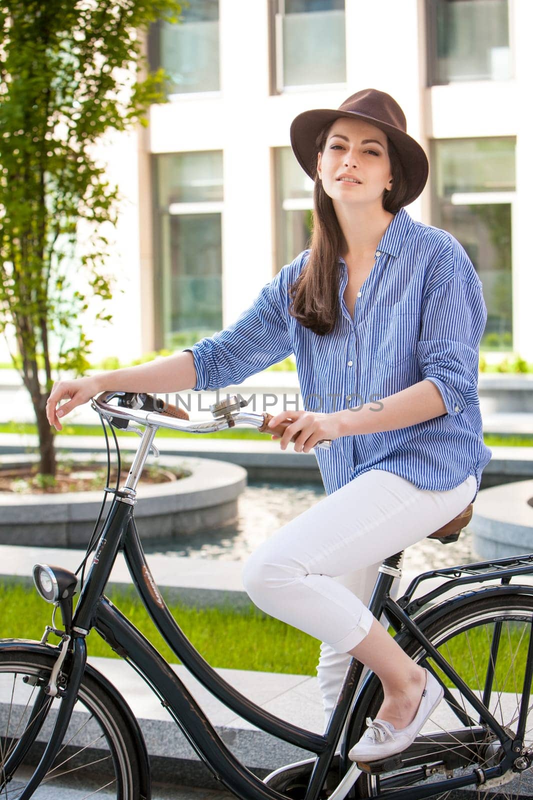 Pretty smiling girl in hat and blue dress riding a bicycle at street