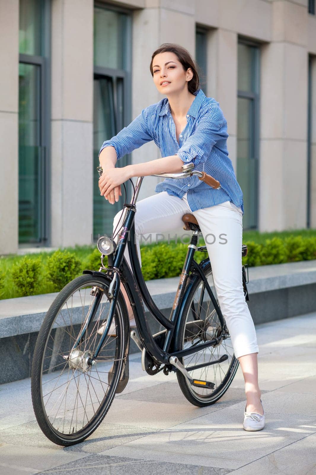 Pretty smiling girl iin blue dress sitting on a bicycle at street