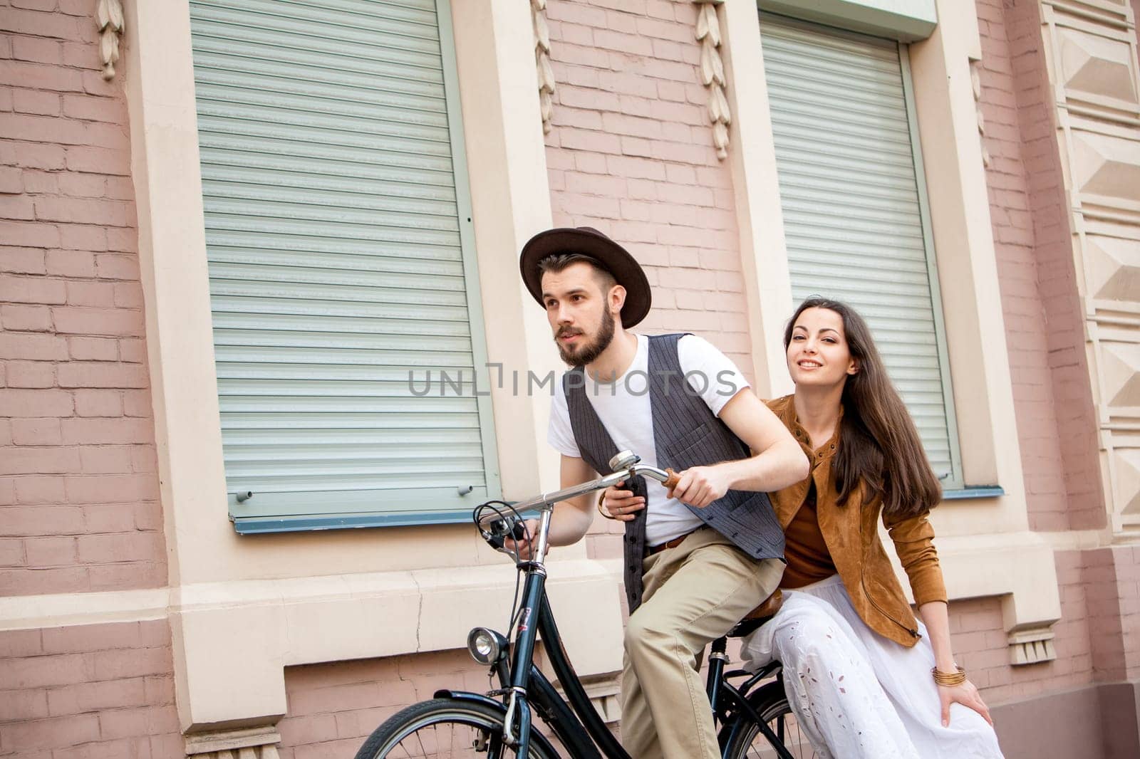 Young couple sitting on a bicycle against the wall in town
