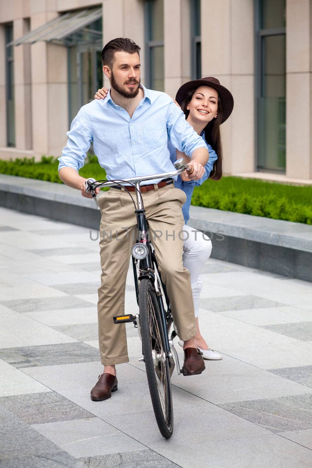 Young couple sitting on a bicycle opposite the green city streets