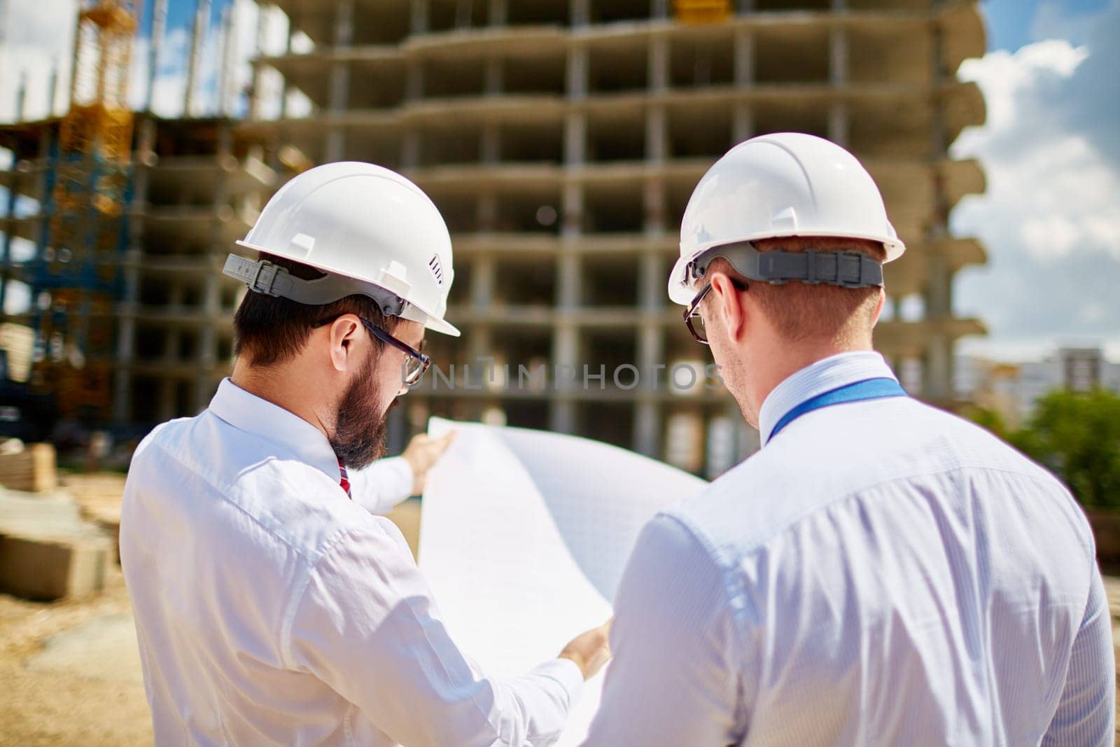 Male architects in helmets discussing sketch of new building