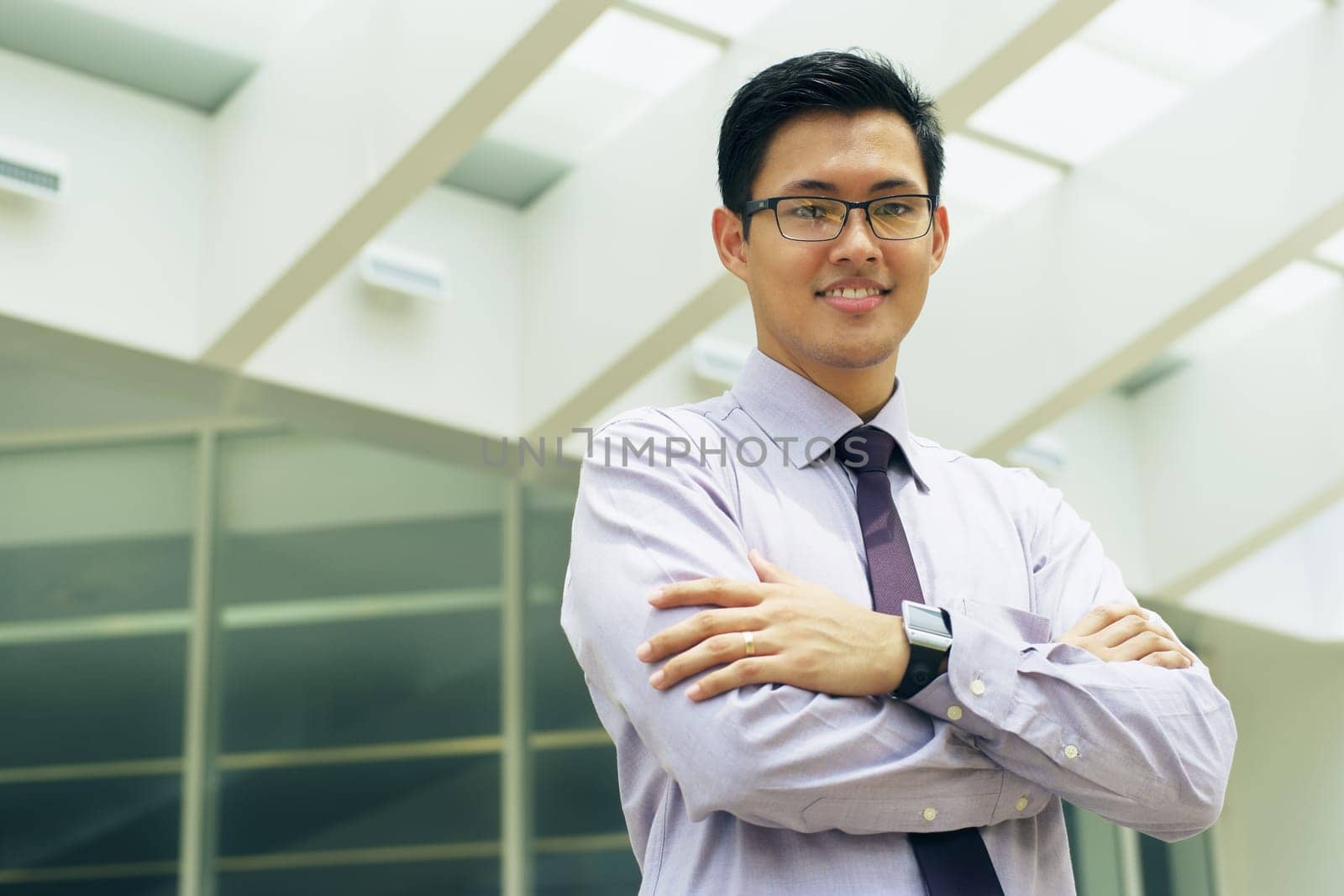 Portrait of happy and confident young asian businessman. The man stands in a street against office buildings and crosses arms looking at camera