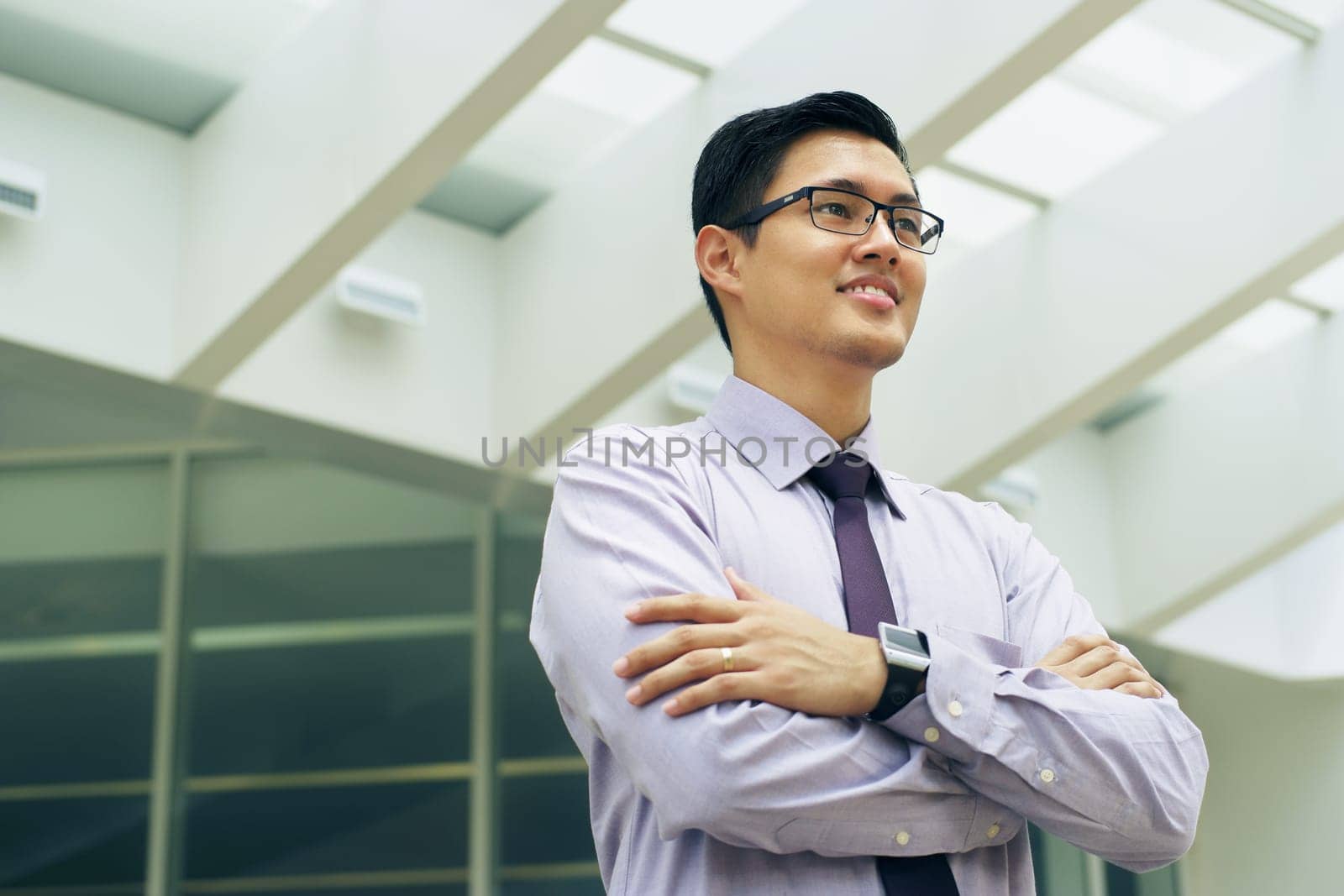 Portrait of happy and confident young asian businessman. The man stands in a street against office buildings and crosses arms looking away