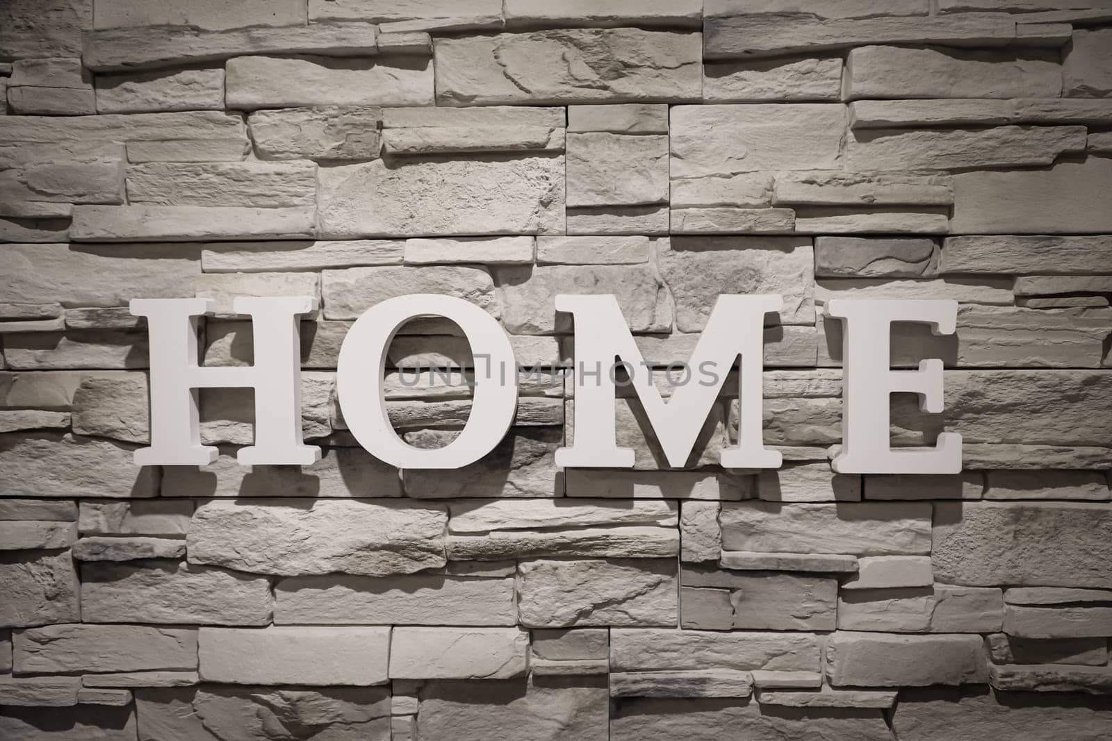 The word "Home"" is written on a wall covered with narrow stones."