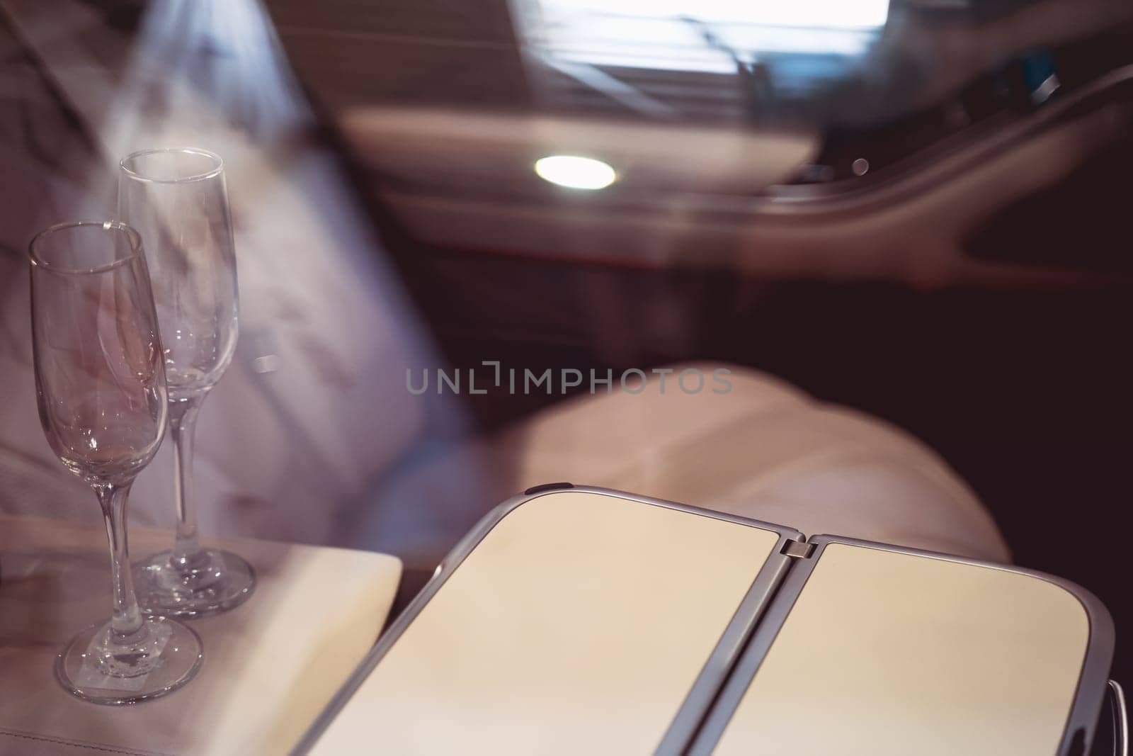 interior of empty luxurious car with brown leather seats and two champagne glasses on arm rest seen through the side window