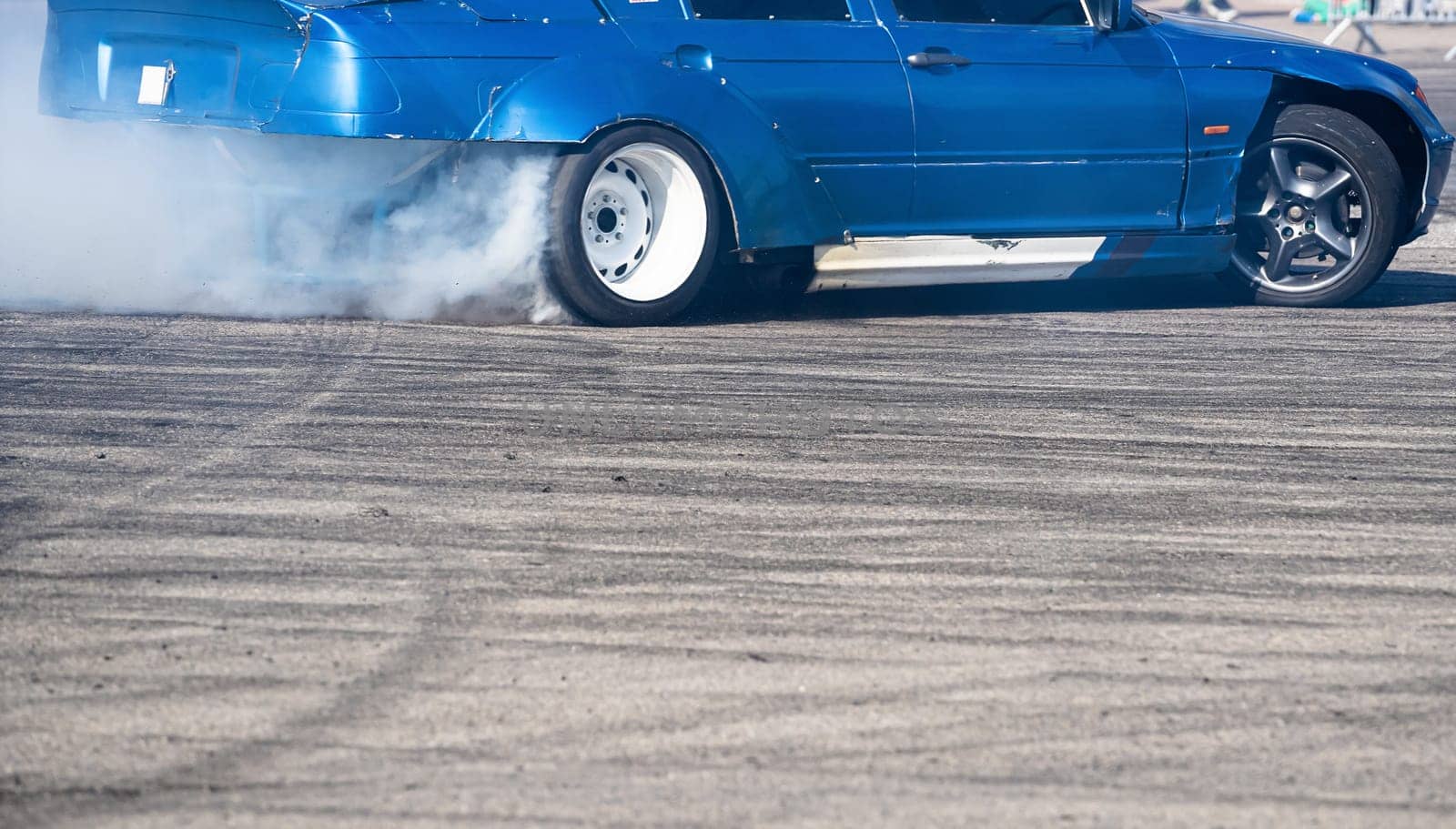 closeup side view of blue sport car drifting on gray speed tarmac track with white smoke coming out of the back tire wheel with copy space available
