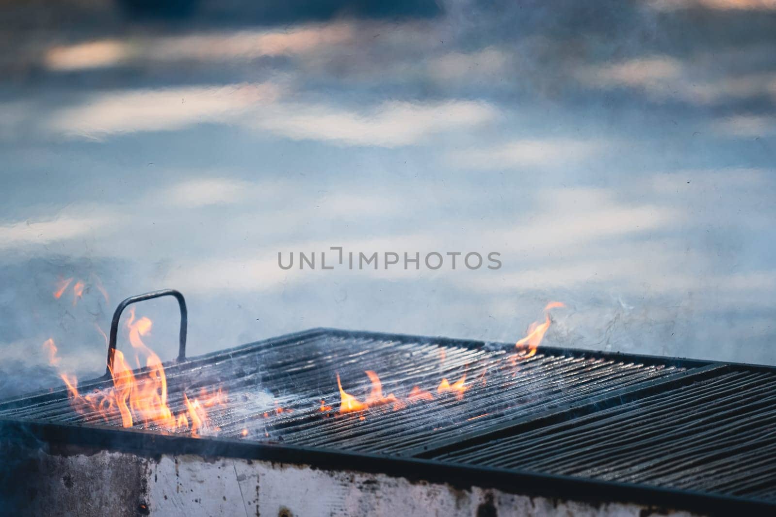 front view closeup detail of metallic large old barbeque grill with fire flames and smoke coming out