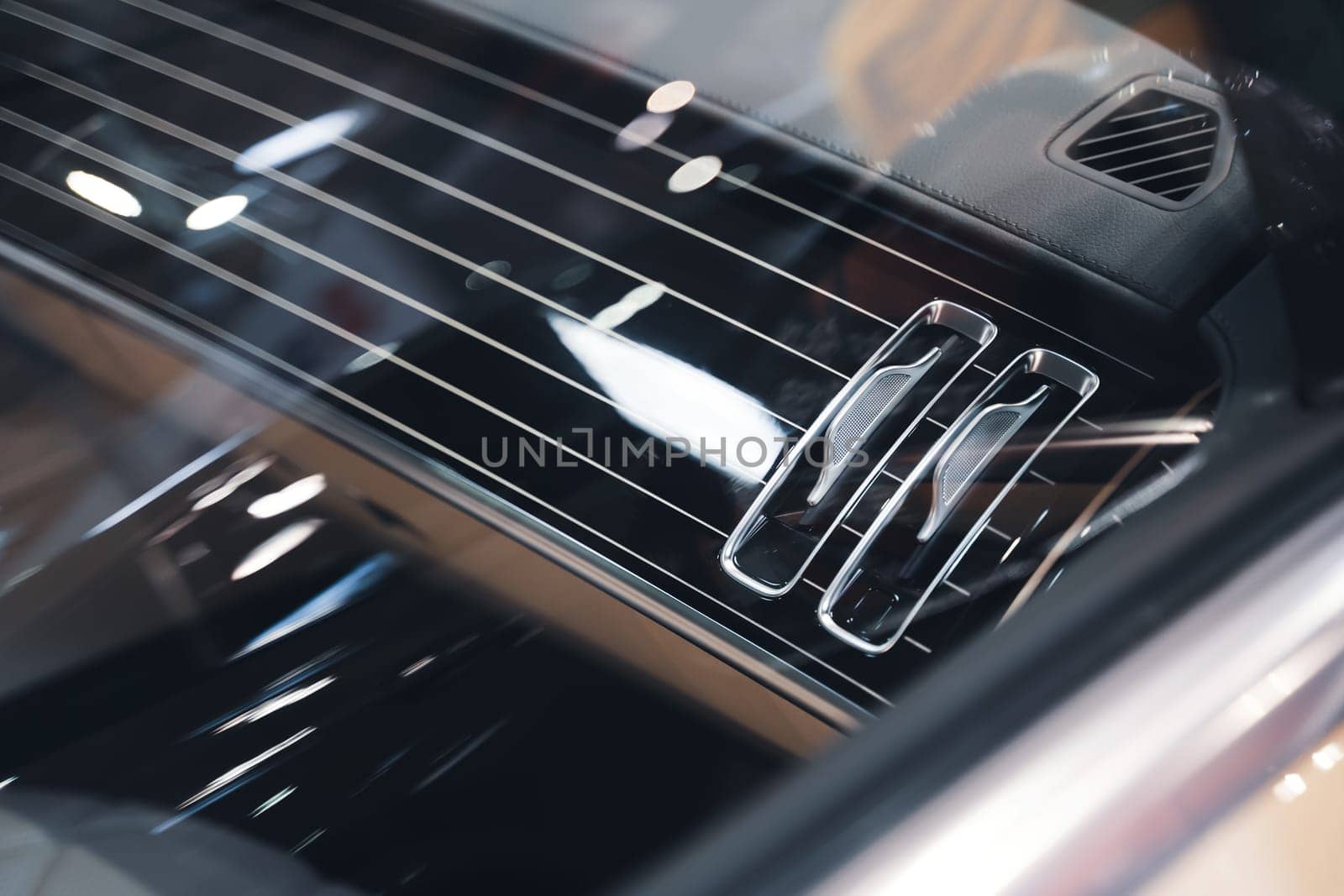 black interior of a luxurious car air conditioning system with leather and shiny chrome dashboard details seen through the side window