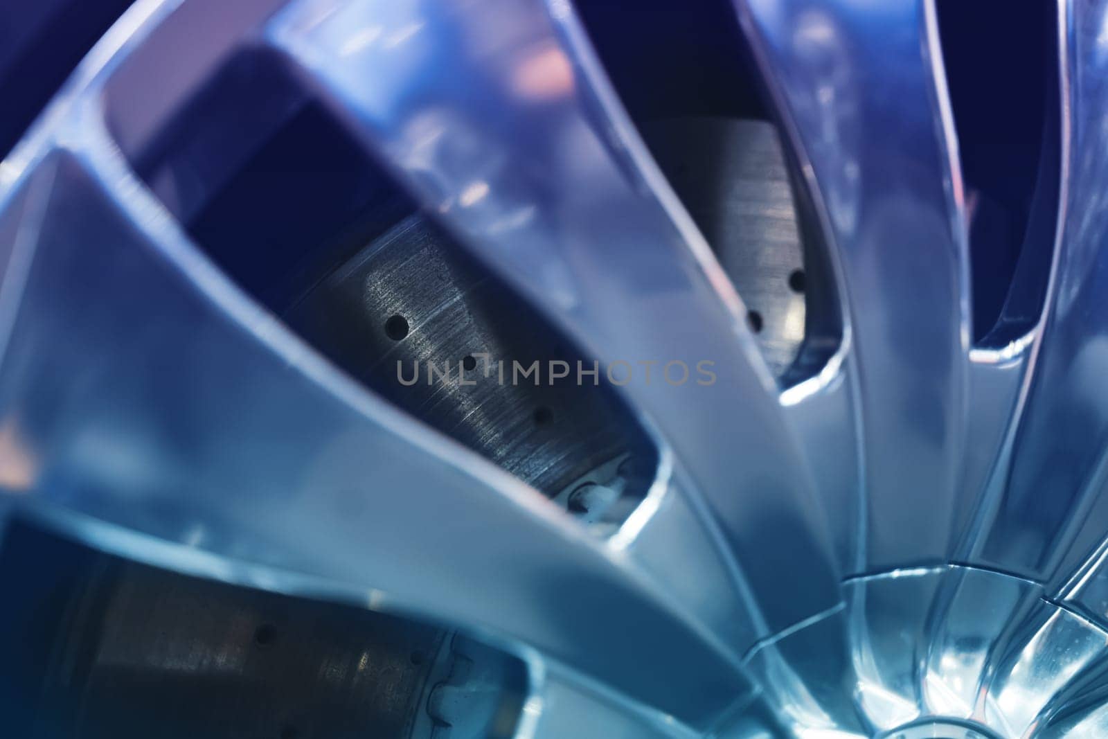 closeup of stationary aerated shiny car disk break with perforation seen through silver chrome rim wheel